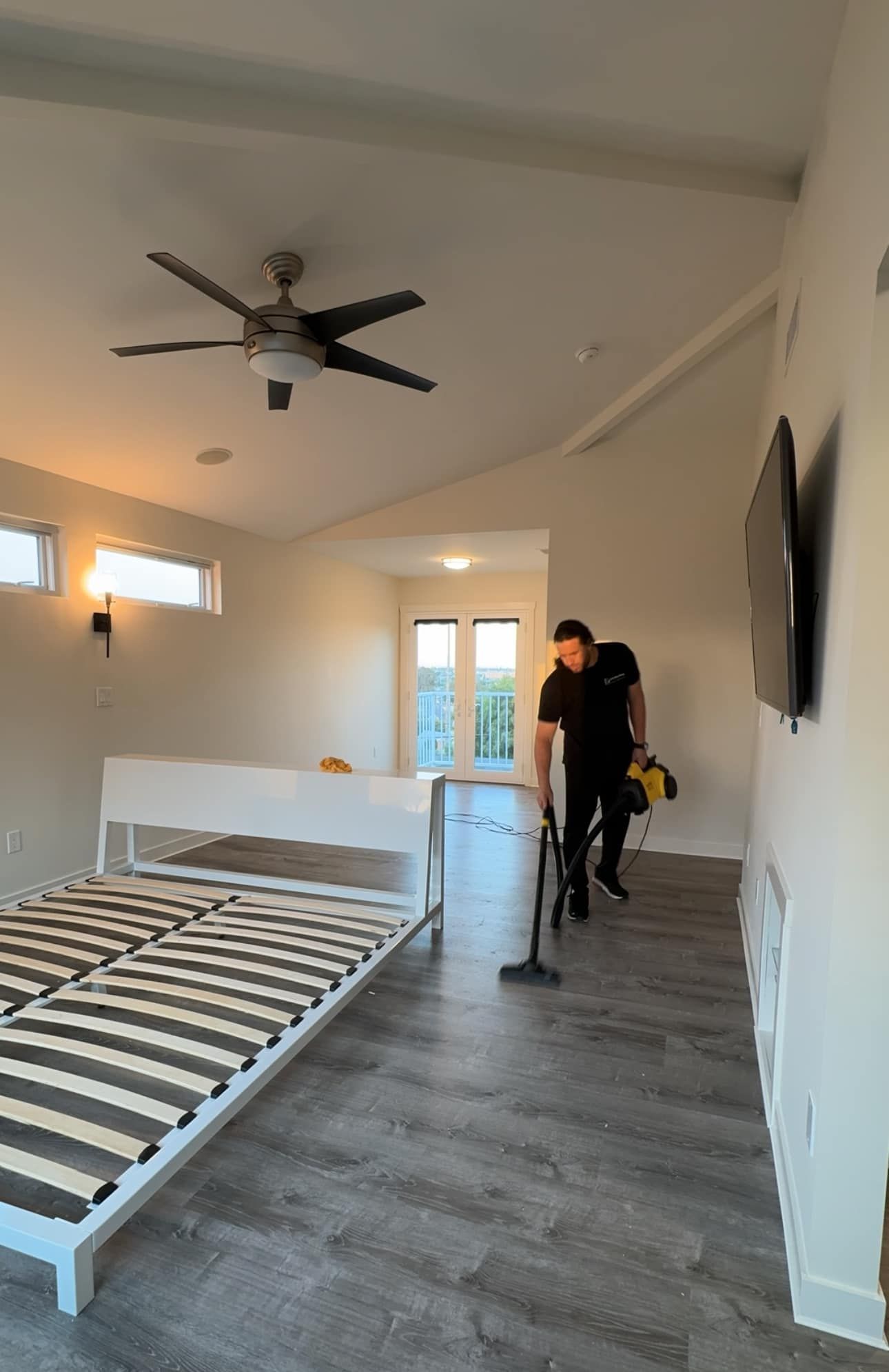 A man is using a vacuum cleaner in a bedroom next to a bed.