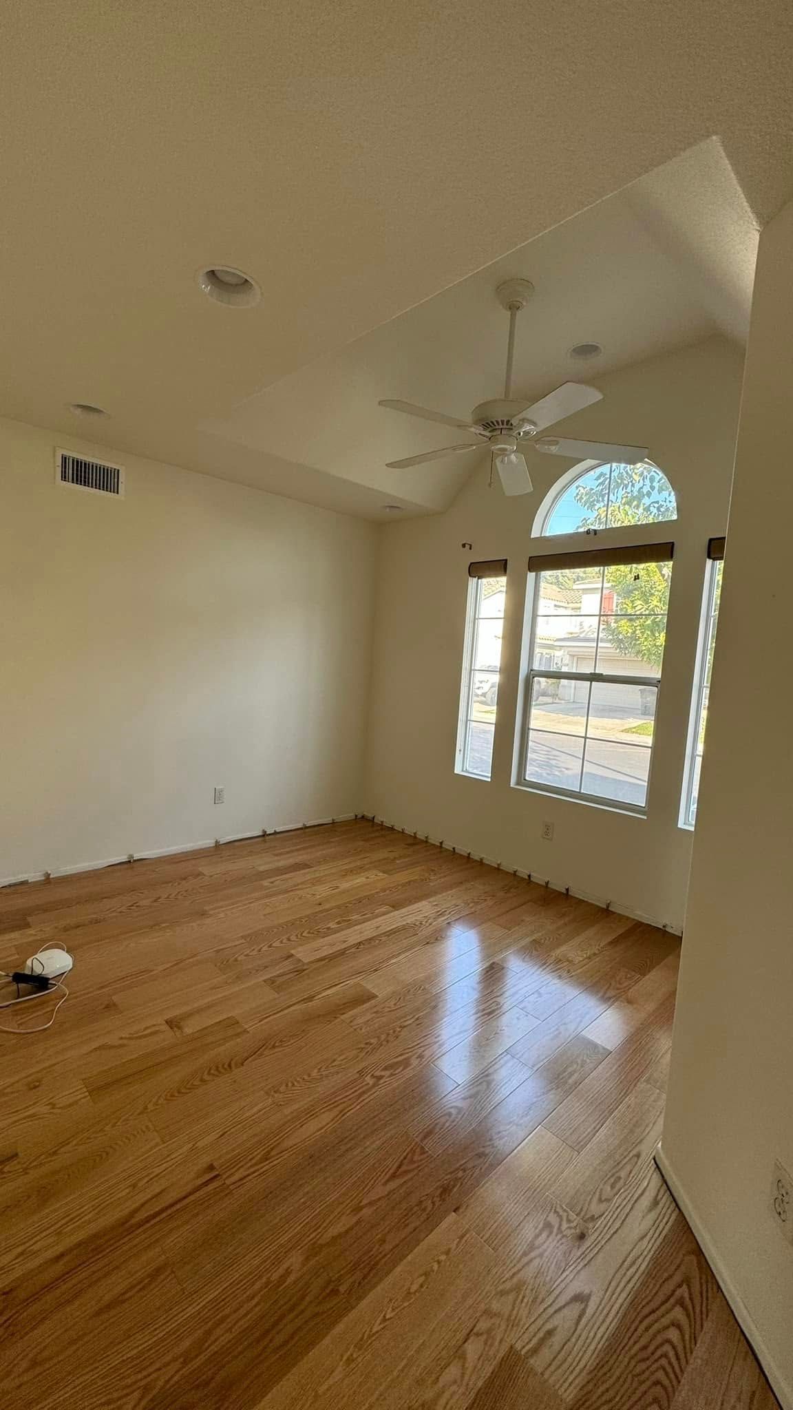 An empty room with hardwood floors and a ceiling fan.