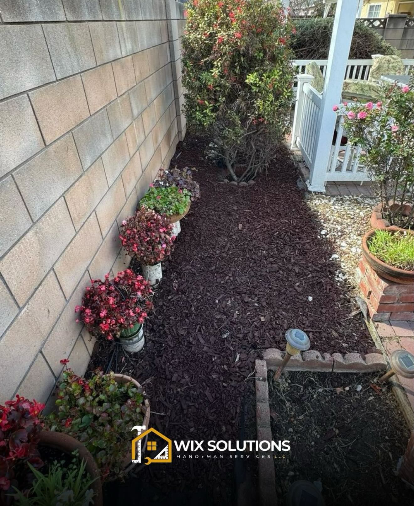 A garden with potted plants and mulch next to a brick wall.