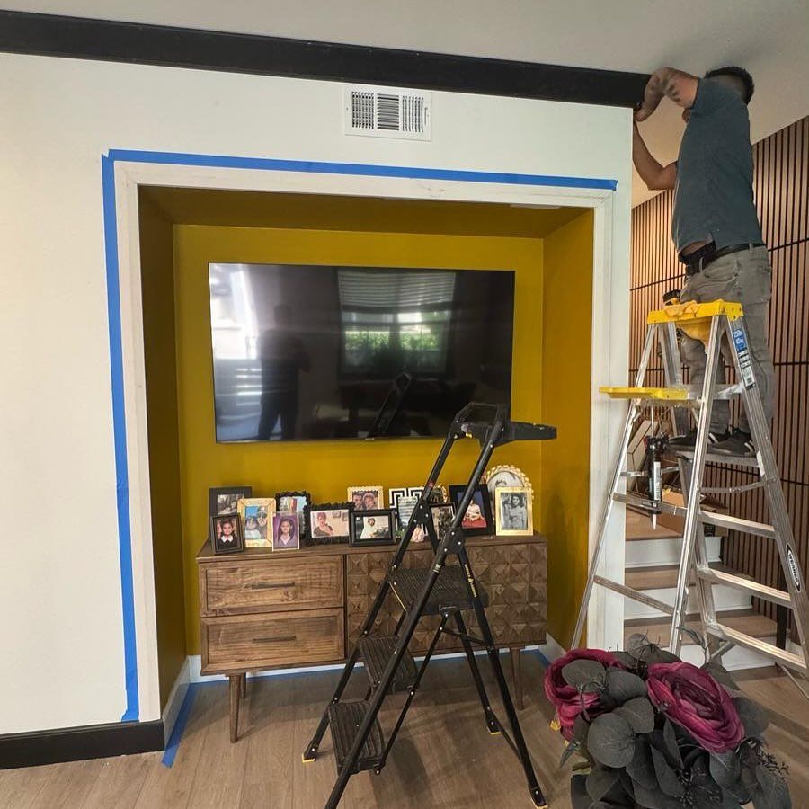 A man is standing on a ladder in front of a television in a living room.