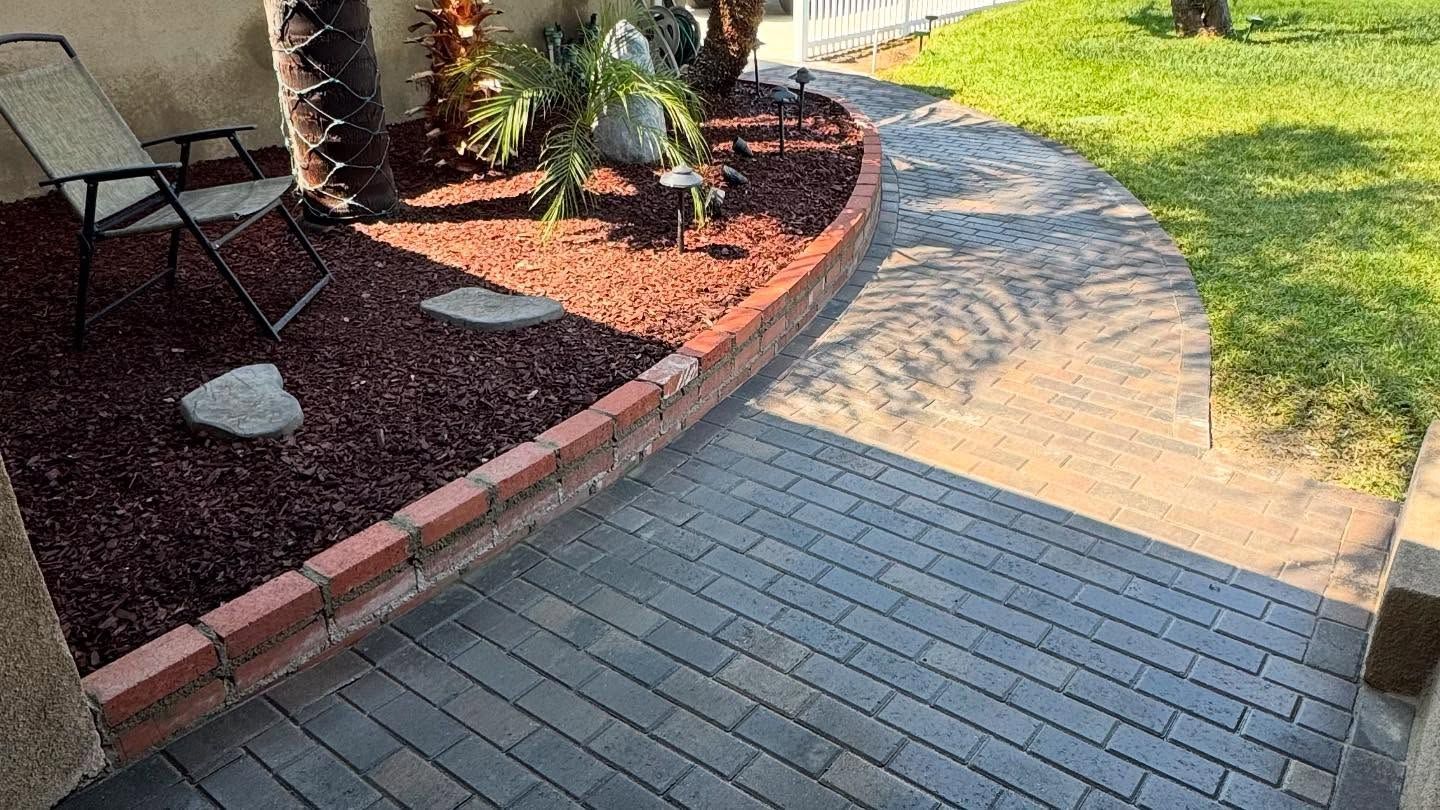 A brick walkway leading to a garden with a chair in the background.