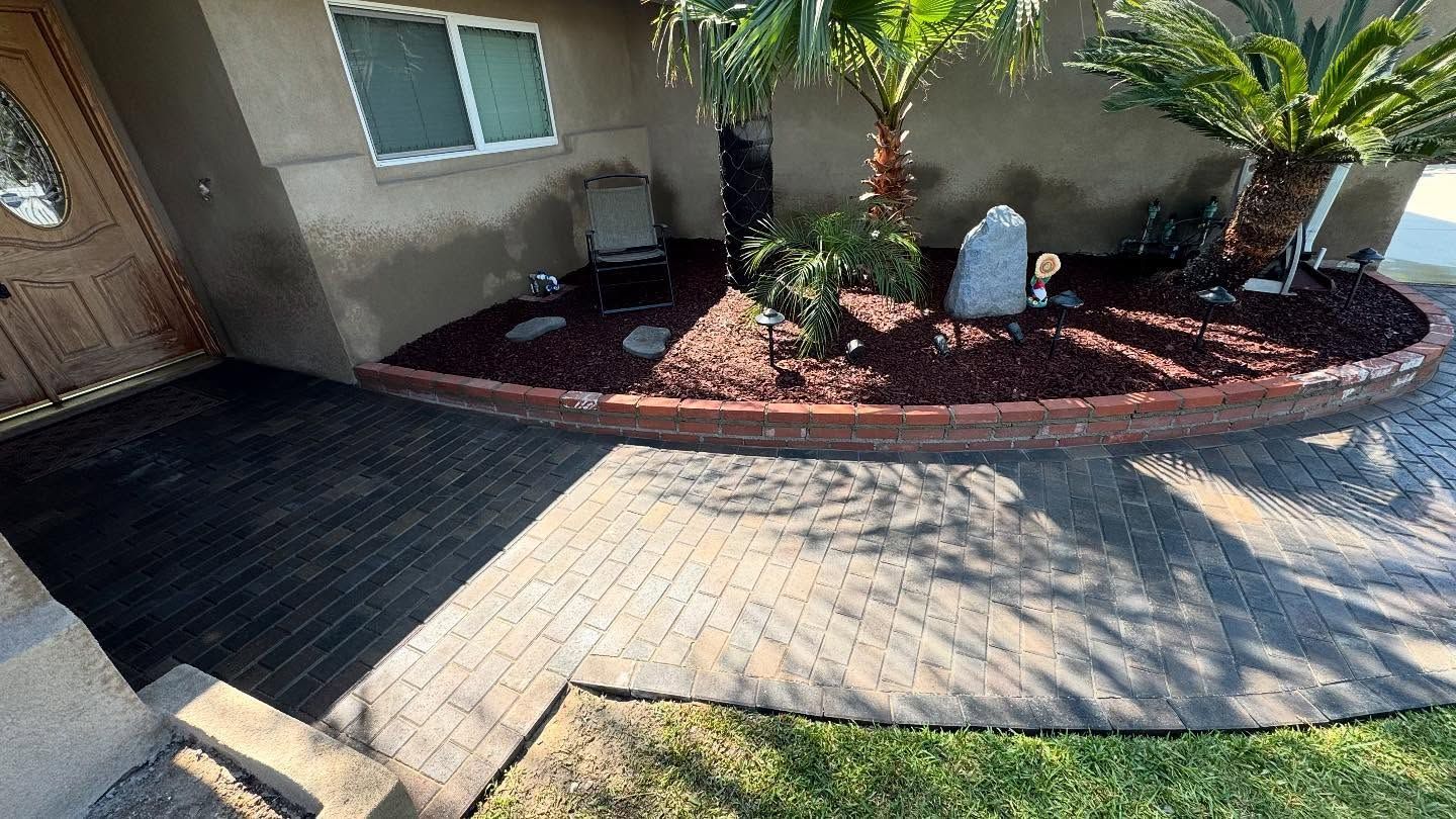 A brick walkway leading to a house with a garden in front of it.