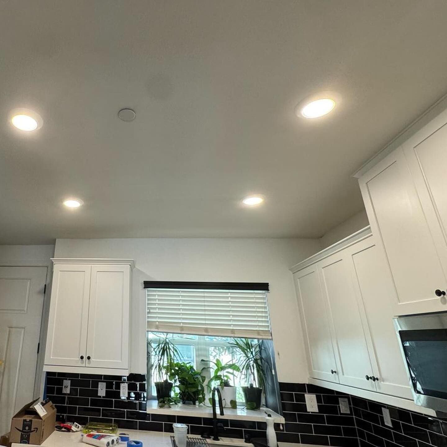 A kitchen with white cabinets and black tiles and a window.