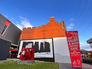A sign for the art gallery and shop is in front of a brick building.