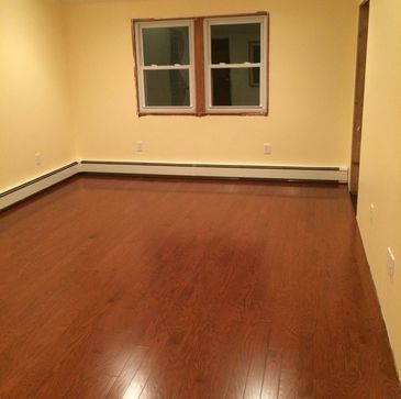 An empty living room with hardwood floors and two windows.