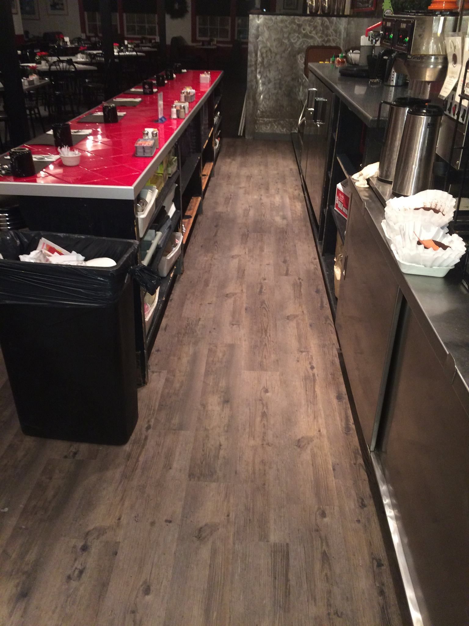 A long hallway in a restaurant with wooden floors and stainless steel counter tops.
