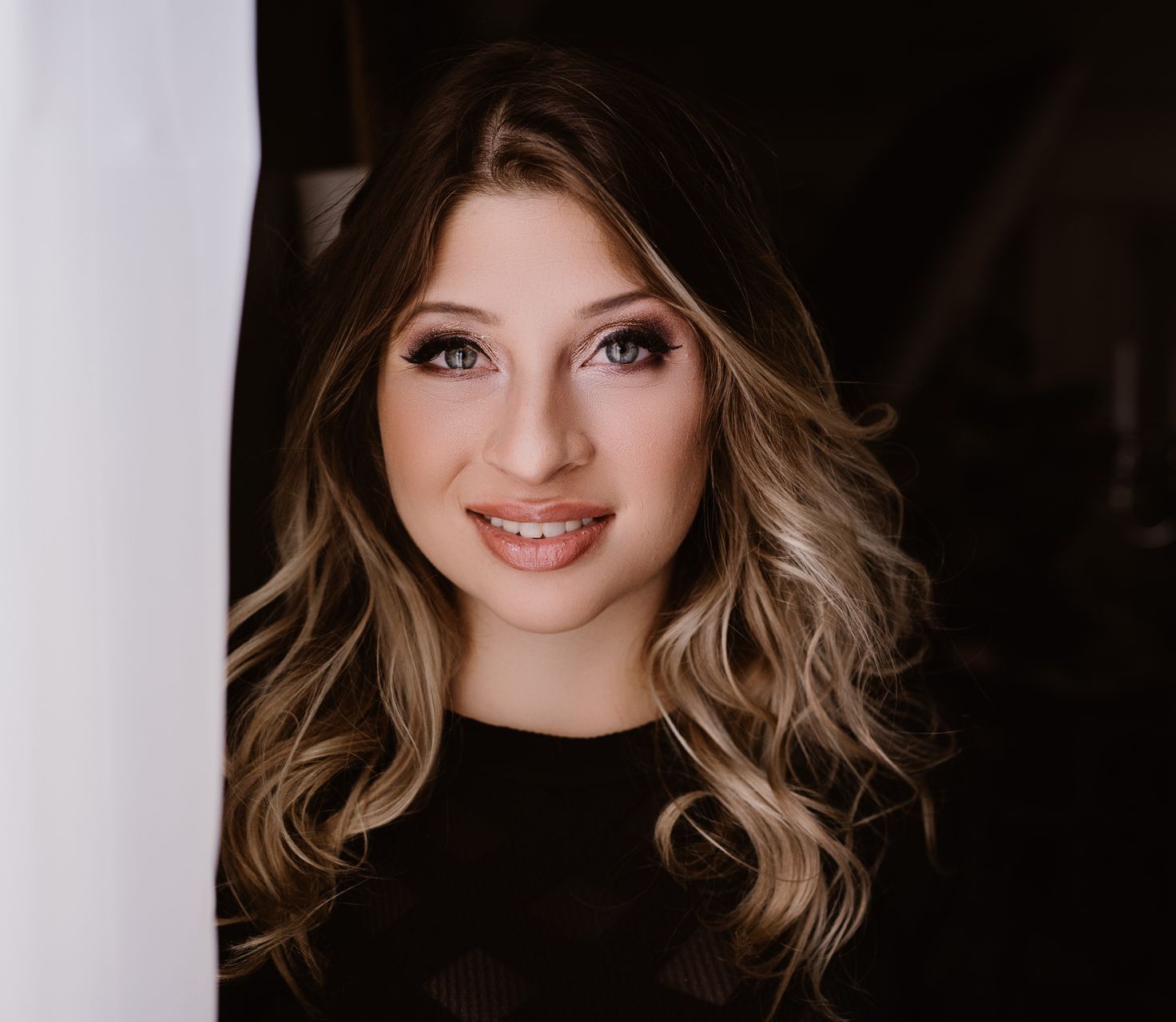 A woman is standing in front of a window and smiling.