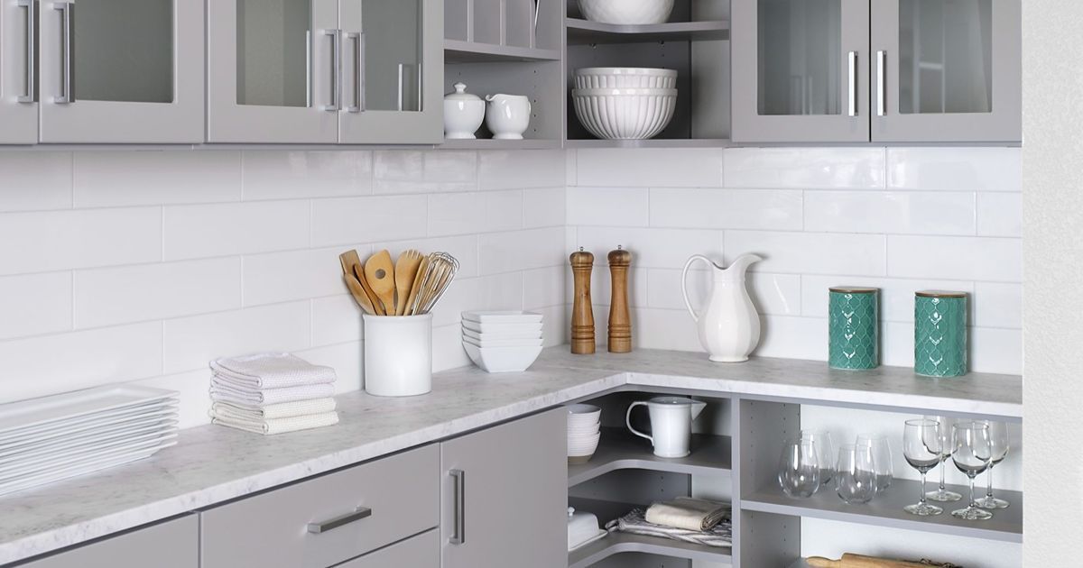 Gray kitchen with white subway tile, cabinets, and countertops, featuring decor and corner shelving.