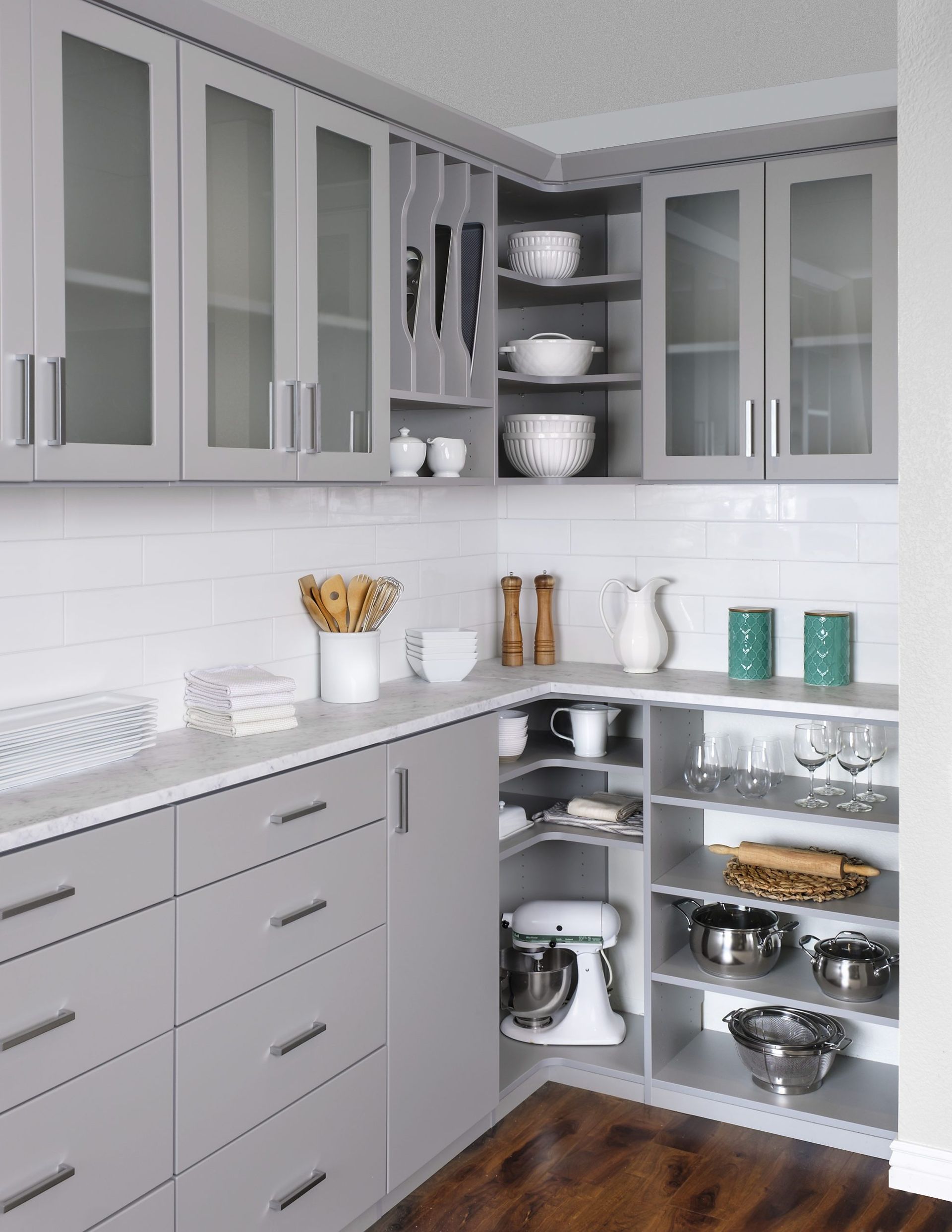 Modern gray kitchen with glass cabinets, white backsplash, and open corner shelves holding dishes and cookware
