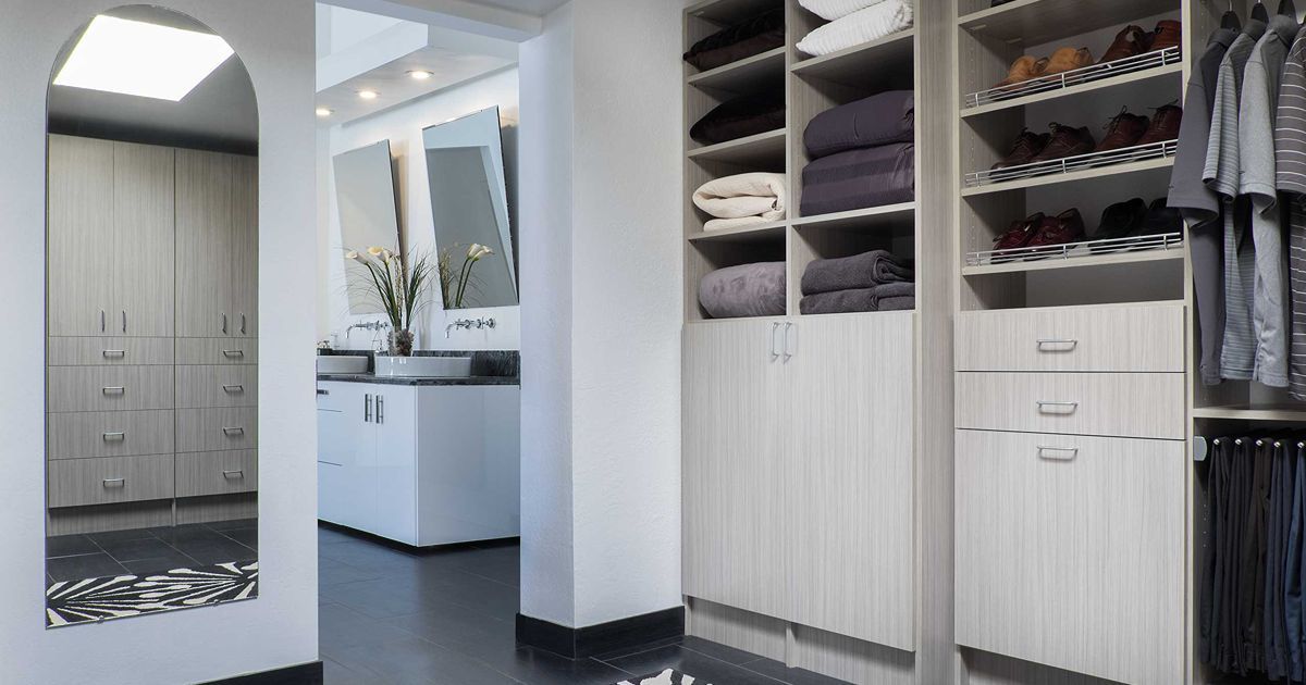 Walk-in closet with shelves, hanging rods, and shoes, connected to a bathroom with sinks and mirrors.