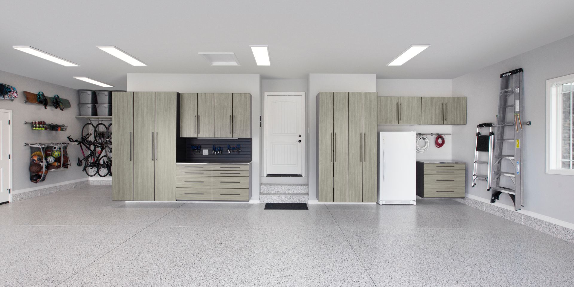 Spacious garage with beige cabinets, white appliances, shelves, and a ladder against the wall