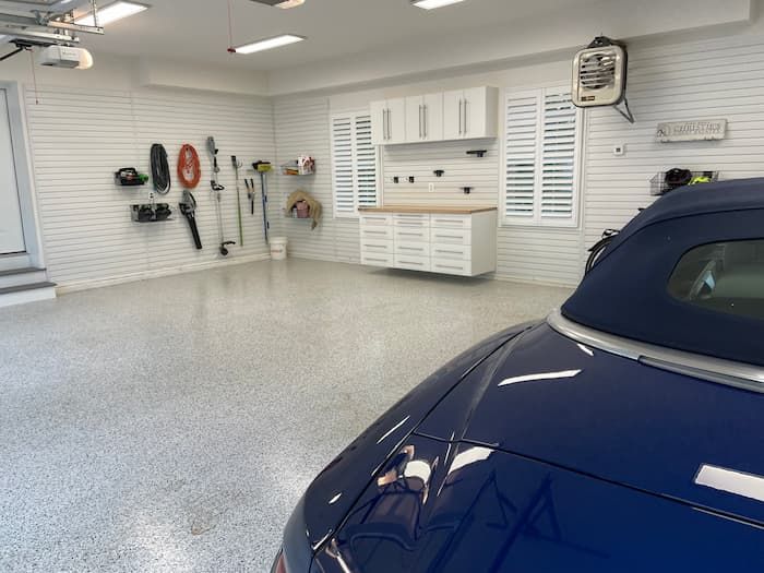 Bright garage with wall-mounted tools and cabinets, and a blue car parked in the foreground