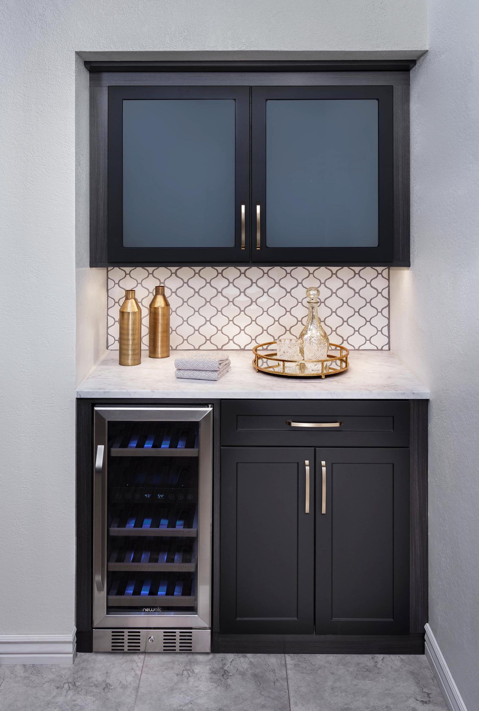 Built-in outdoor bar with dark cabinets, mini fridge, and decorative countertop against a gray wall