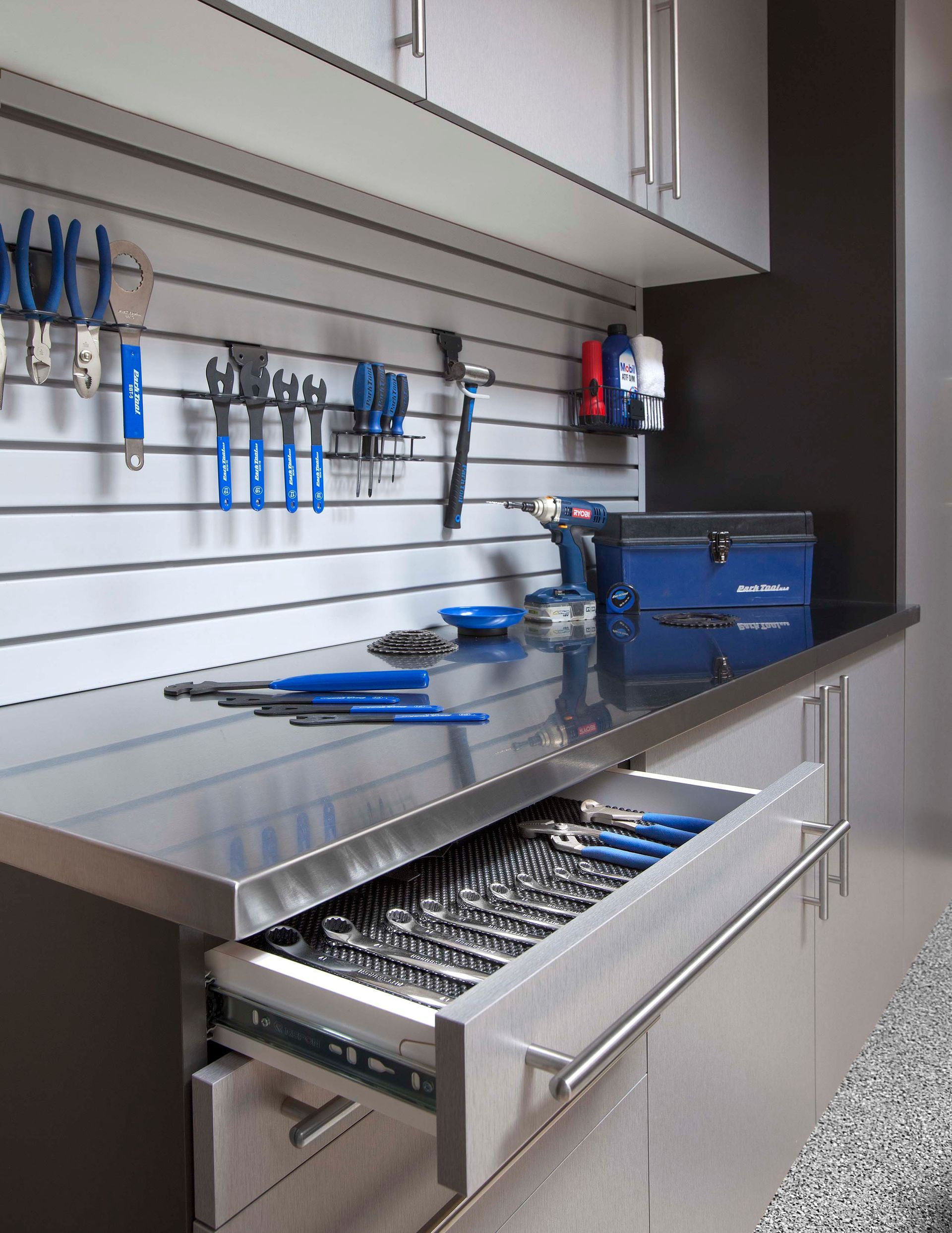 Tool bench with drawers, blue-handled tools on wall, and a blue toolbox on a stainless steel work surface.