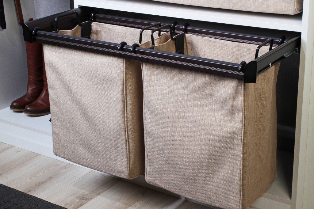 Black metal storage bench with beige fabric bins beside a person’s boots