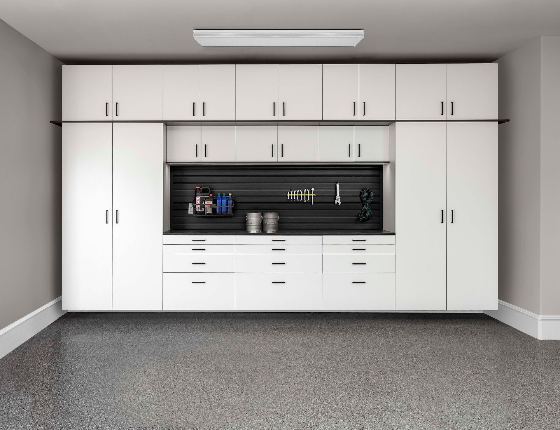 White garage cabinets and workbench with a black backsplash on a gray carpeted floor