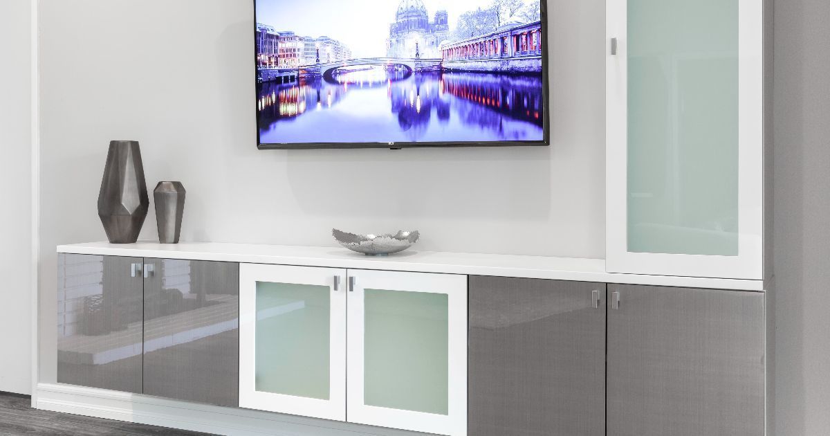 Modern living room with wall-mounted TV, white cabinets, gray sideboard, and decorative vases