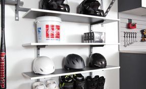 Shelves in a garage holding helmets, shoes, and a red-and-white cup on the top shelf