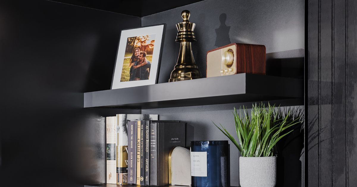 Black bookshelf with framed photo, books, small Eiffel Tower ornament, clock, and potted plant