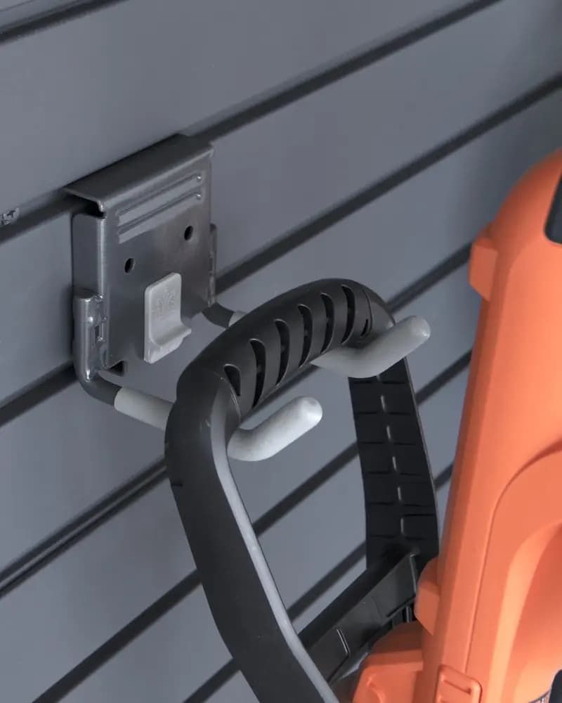 Wall-mounted holder with a black loop handle beside orange equipment on a gray paneled wall