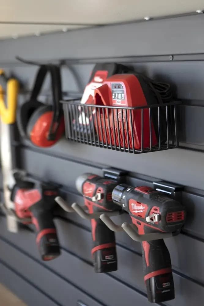 Cordless power tools stored on a wall-mounted rack in a garage or workshop.