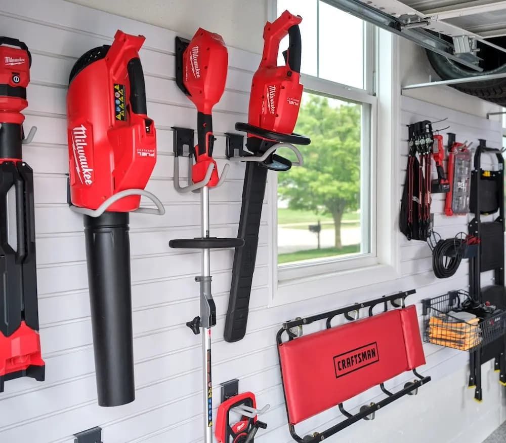 Red Milwaukee power tools and accessories neatly mounted on a white wall in a bright garage.