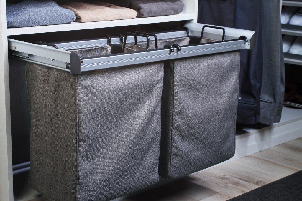 Gray fabric laundry hamper with two compartments, mounted in a closet. The hamper is pulled out on a track.