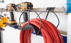 Red coiled extension cord hanging on a wall rack next to power drills.
