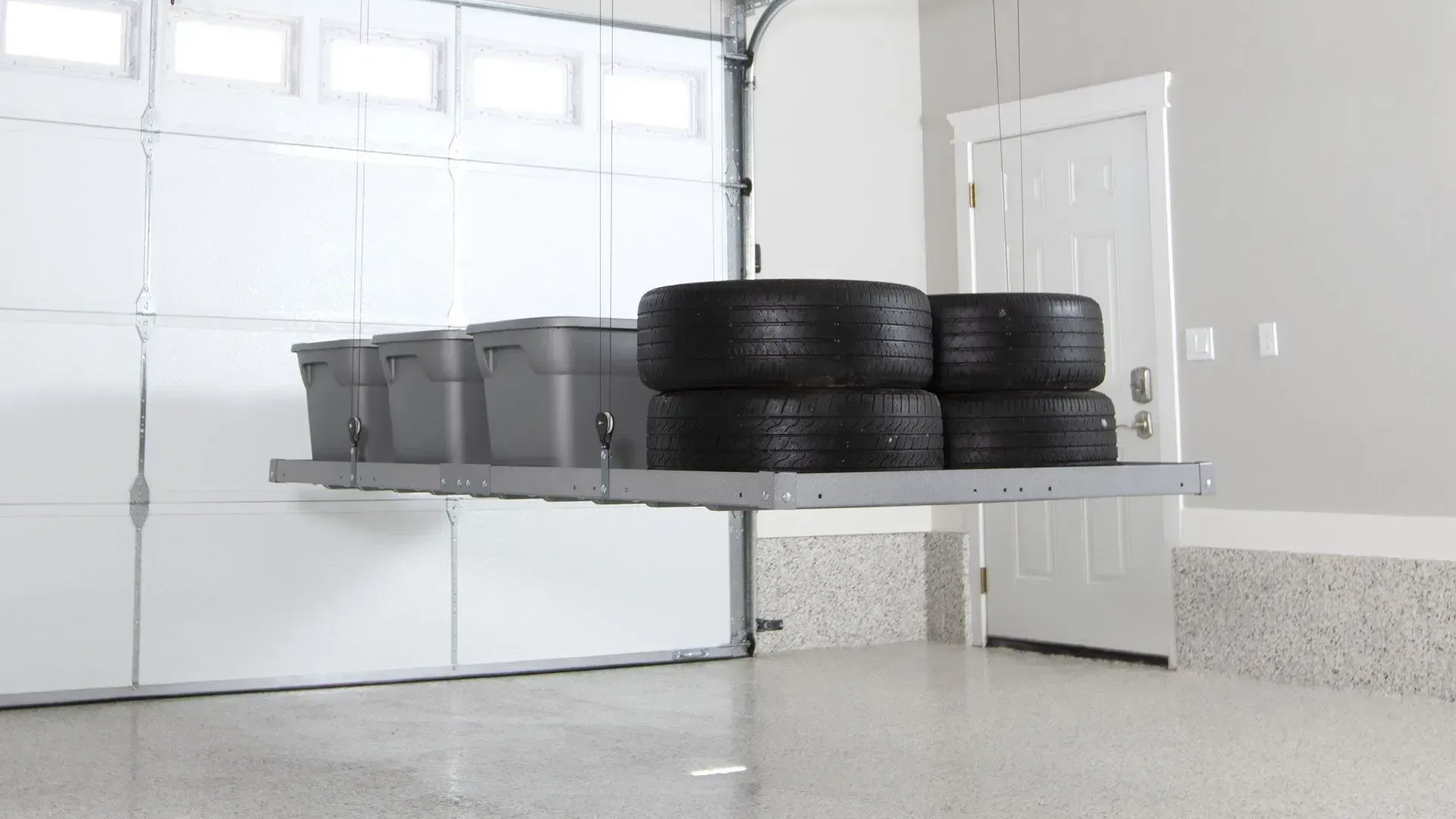 Stacked tires and bins on a raised platform in a clean garage with white doors