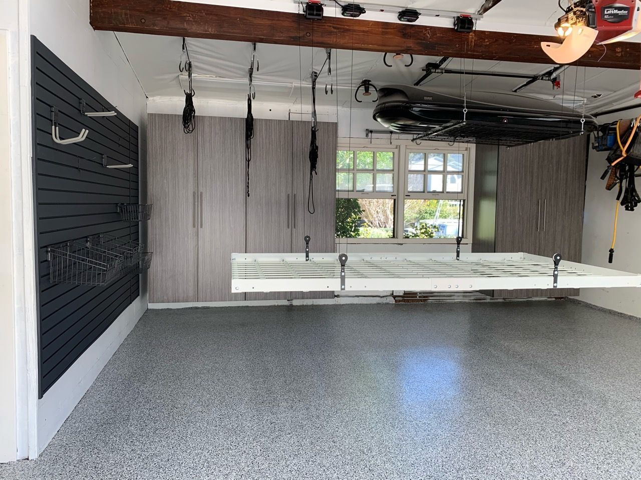 Empty garage with gray floor, exposed ceiling beams, and hanging ropes or cables near a window.