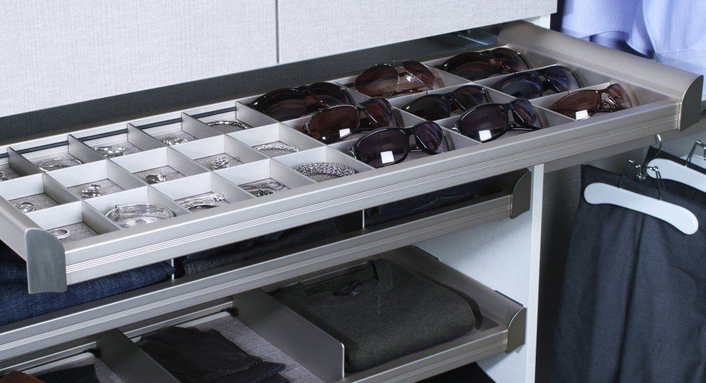 Organized tray of assorted watches and accessories on a shelf beside hanging clothes