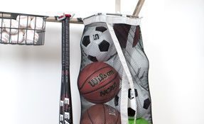 Basketballs and a soccer ball stored in a white mesh hanging organizer indoors