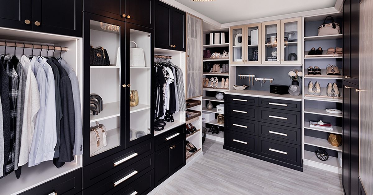 Modern walk-in closet with black cabinetry, glass-front shelves, hanging clothes, and drawers
