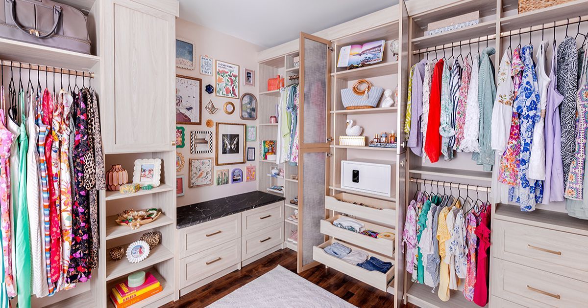 Bright walk-in closet with colorful hanging clothes, shelves, drawers, and wall art