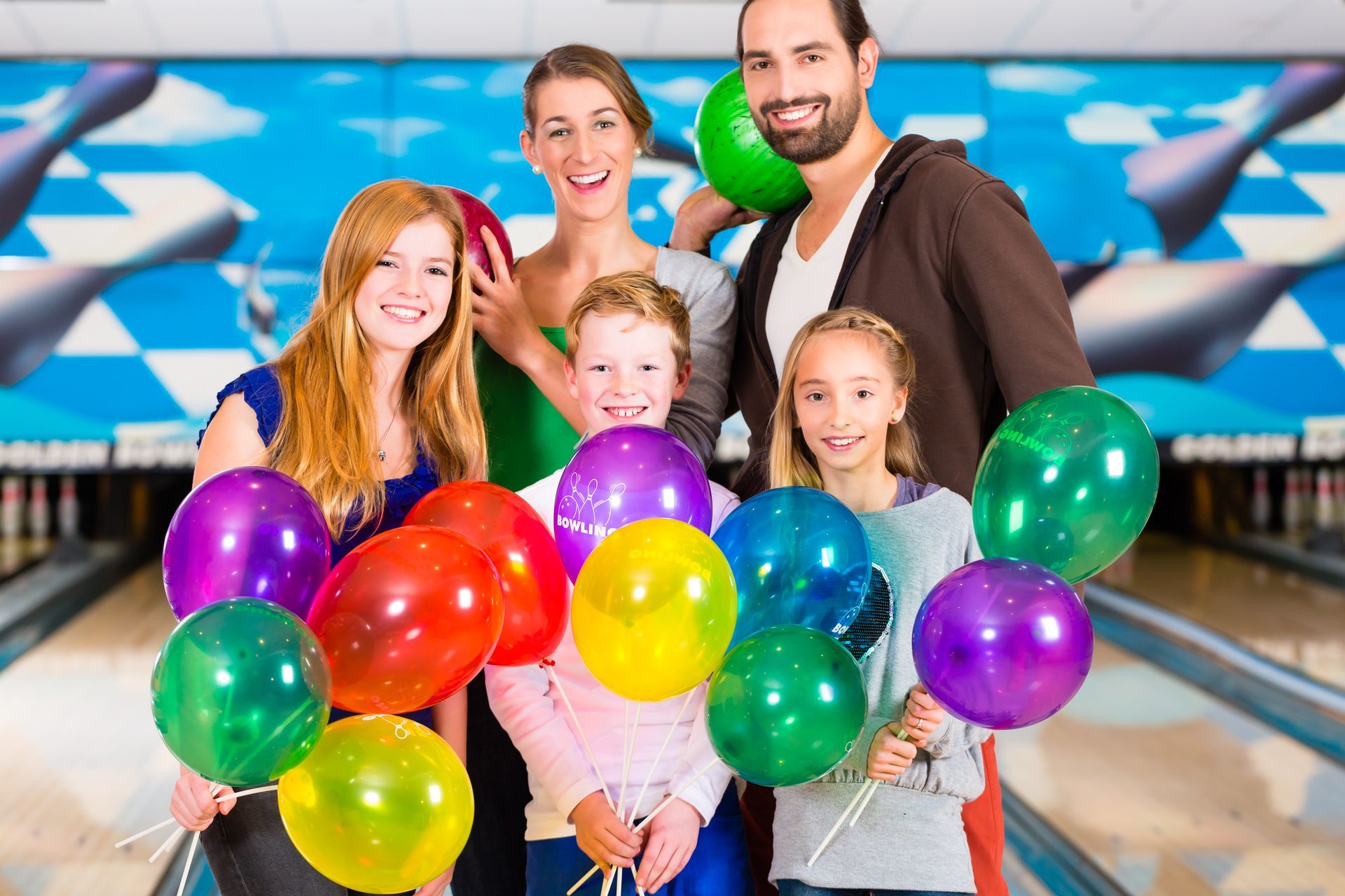 Group of kids holding colorful balloons while celebrating a birthday at a bowling alley.