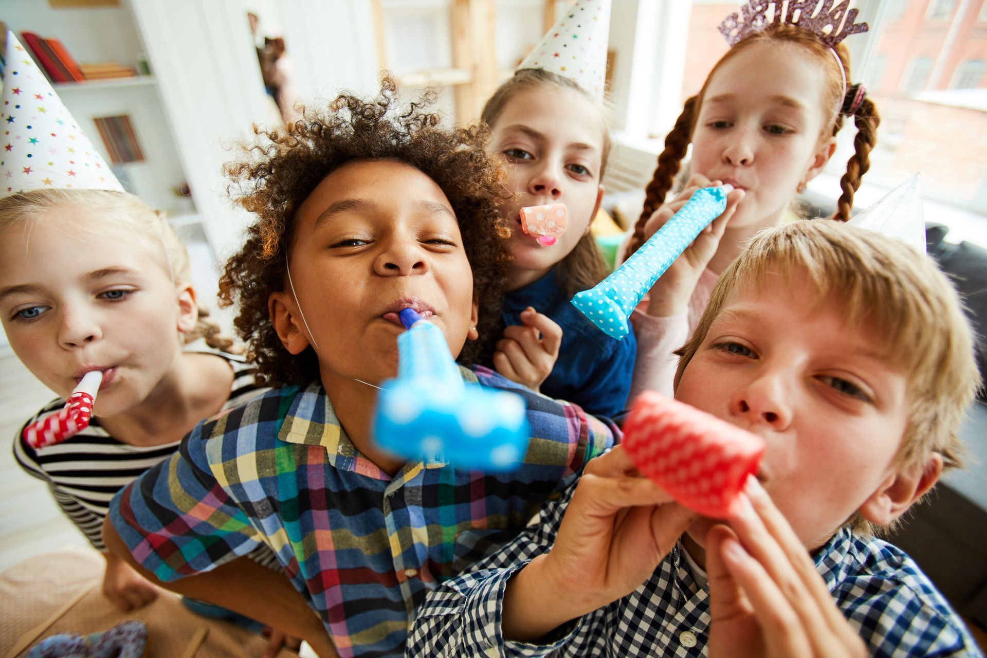 A group of happy children blow party horns at the camera.