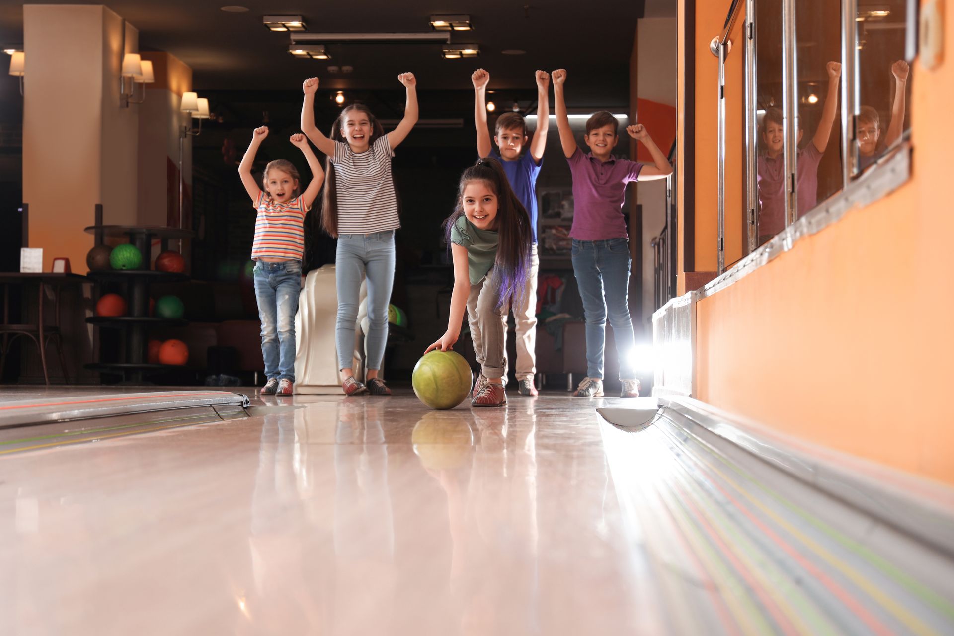 A group of children cheer on a girl as she throws a bowling ball. A group of children cheer on a girl as she throws a bowling ball.