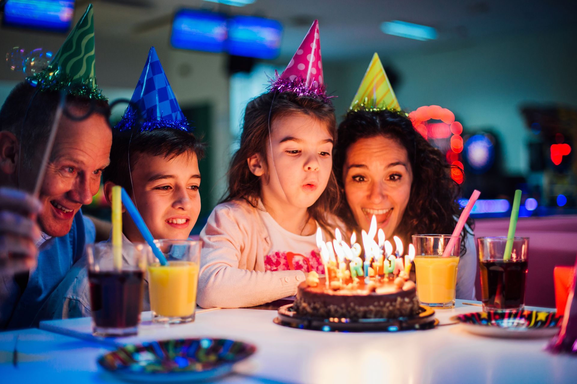 A little girl is blowing candles on a cake with her family in a bowling center.