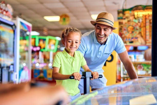 Smiling parent with son on a coin-operated ride inside a lively arcade.