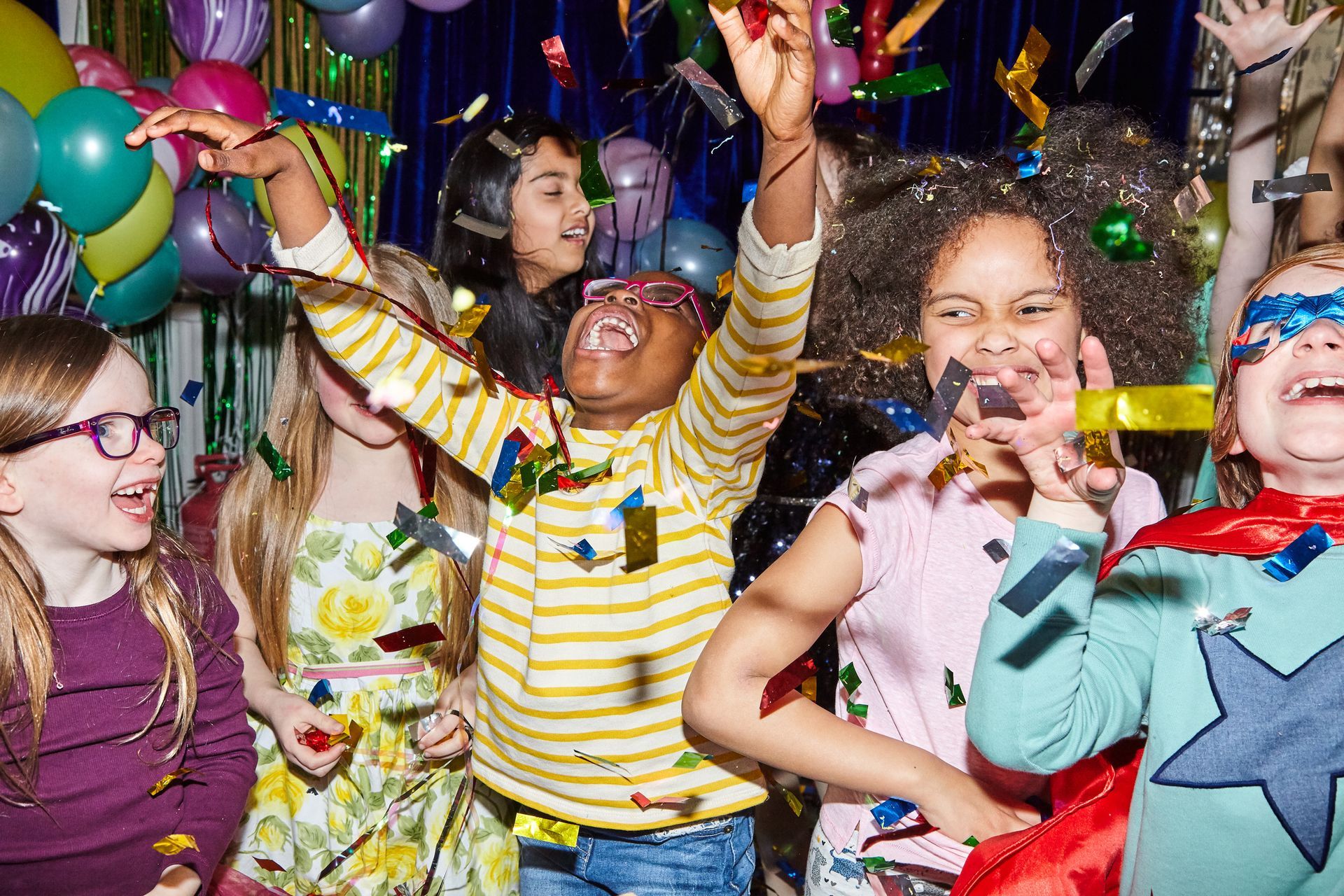 Children’s party service with kids dancing and throwing confetti at colorful indoor celebration.