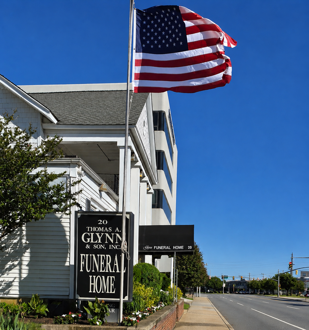 Single-story building with a U.S. flag, landscaped entrance, and covered driveway under a clear sky