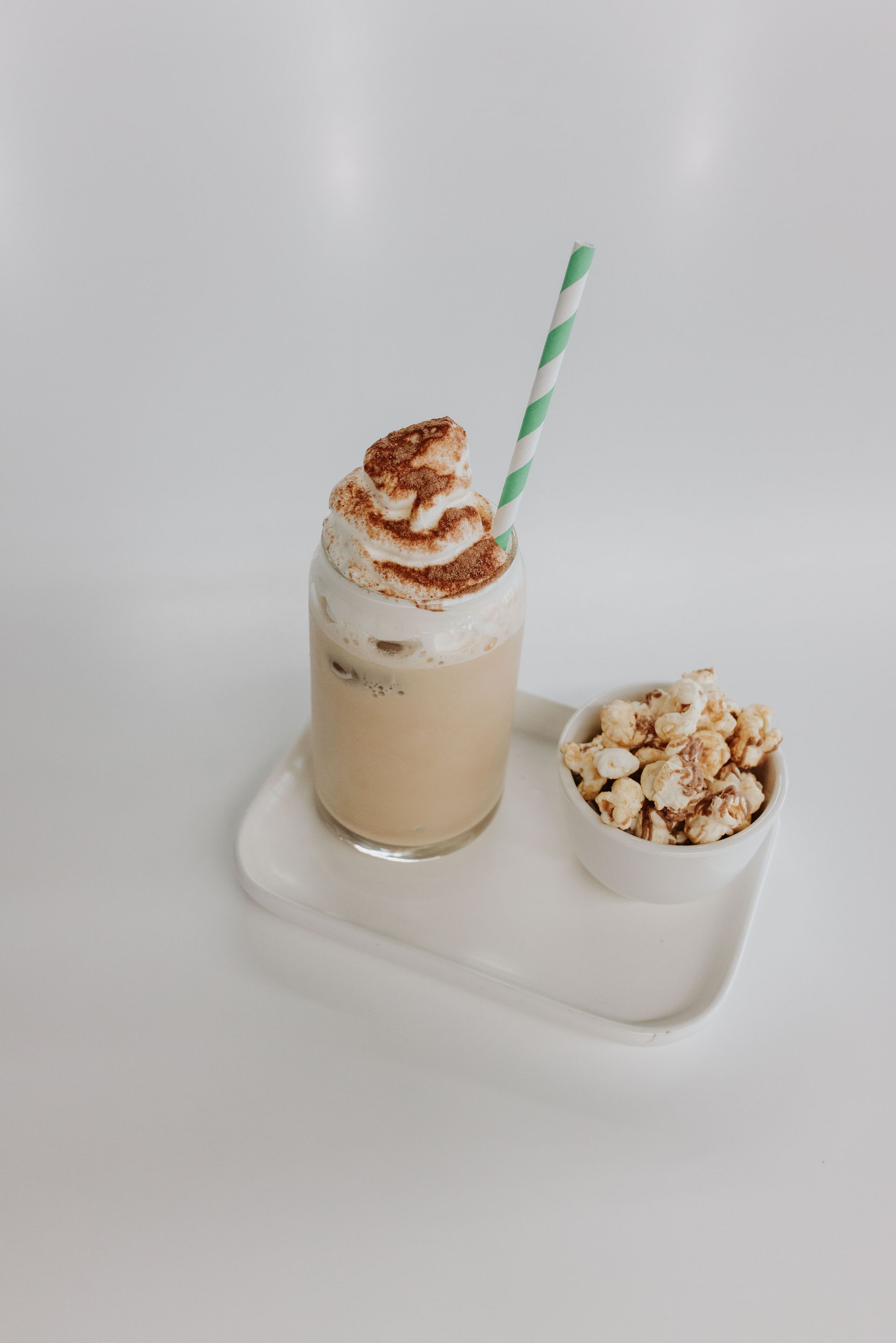 A milkshake with whipped cream and a straw is on a tray next to a bowl of popcorn.