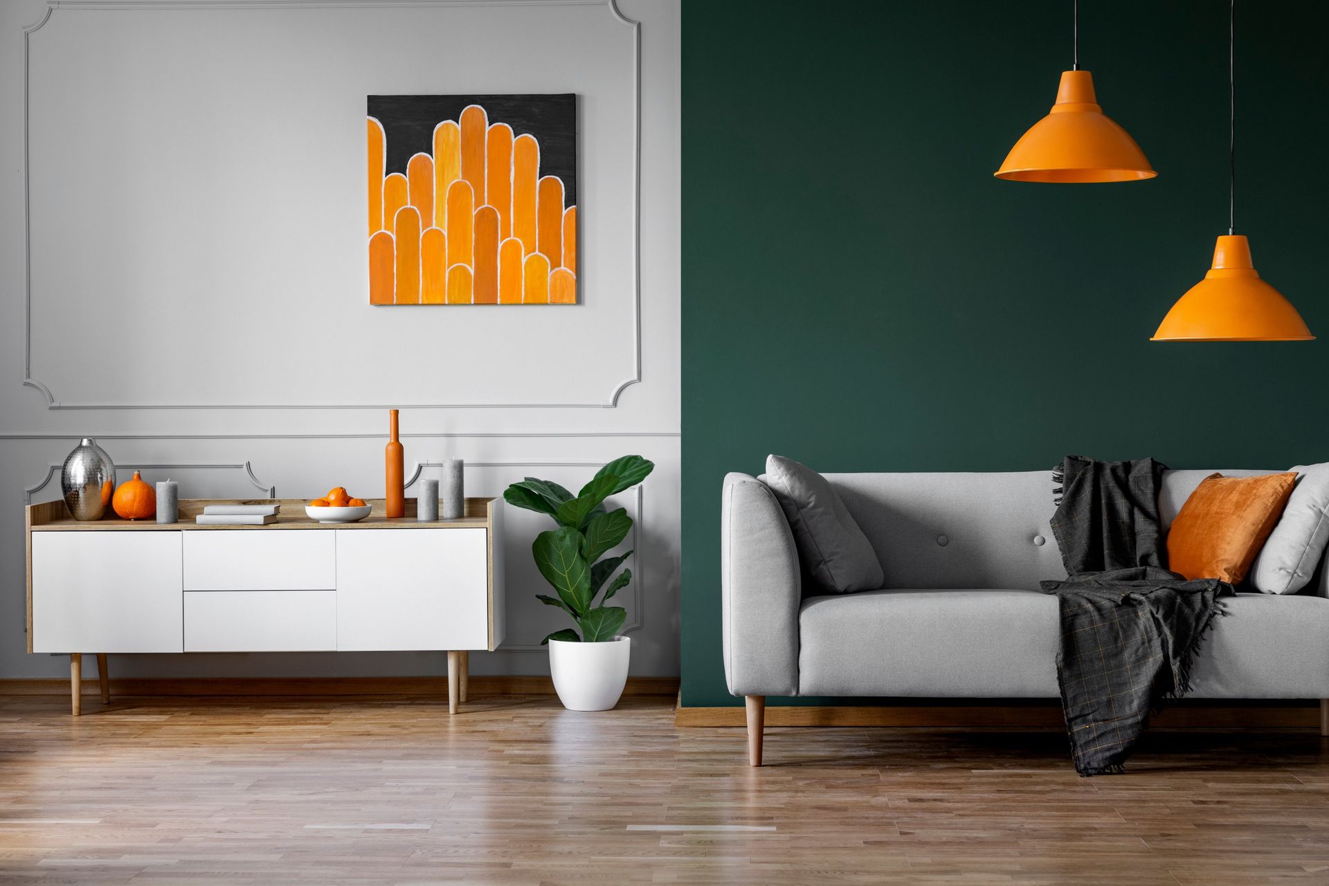 Modern living room with a gray sofa, orange pendant lights, and a white sideboard against a dark green wall.