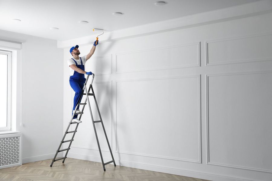 Worker on a ladder painting a white ceiling in a bright room