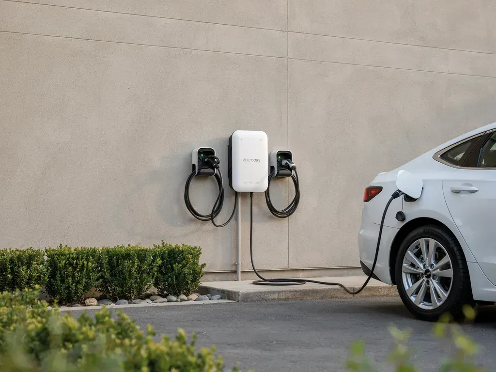 Electric car charging station mounted on a wall beside a silver sedan in a parking lot