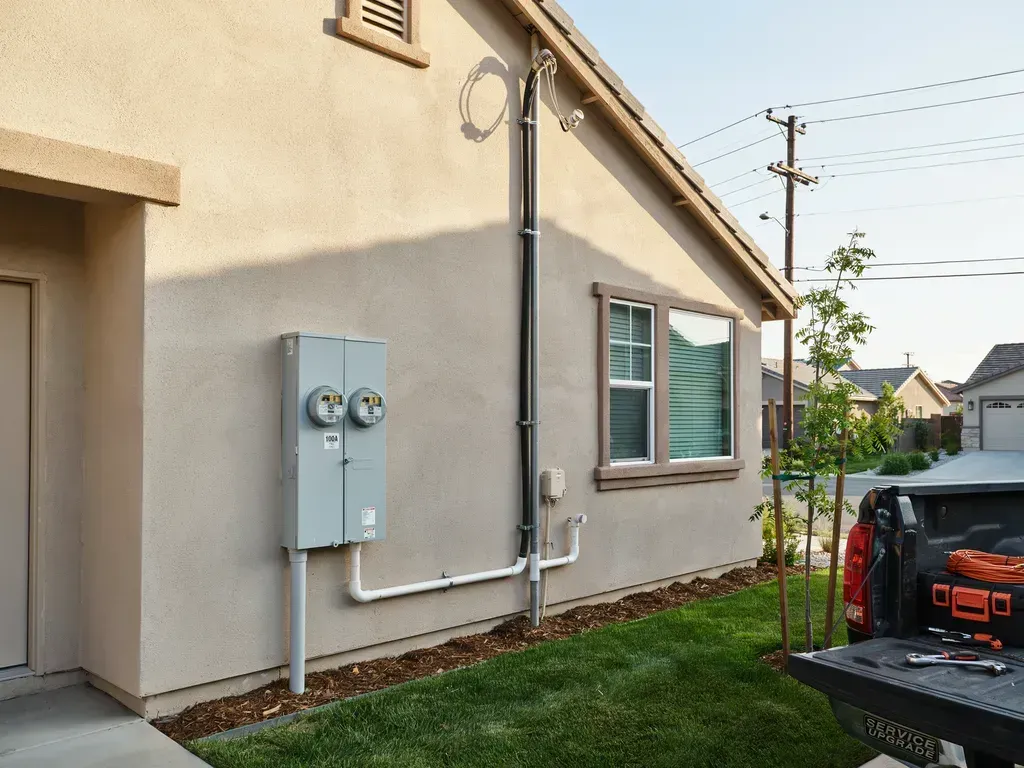 Side view of a beige house with utility meters, a grassy yard, and a parked black pickup truck.