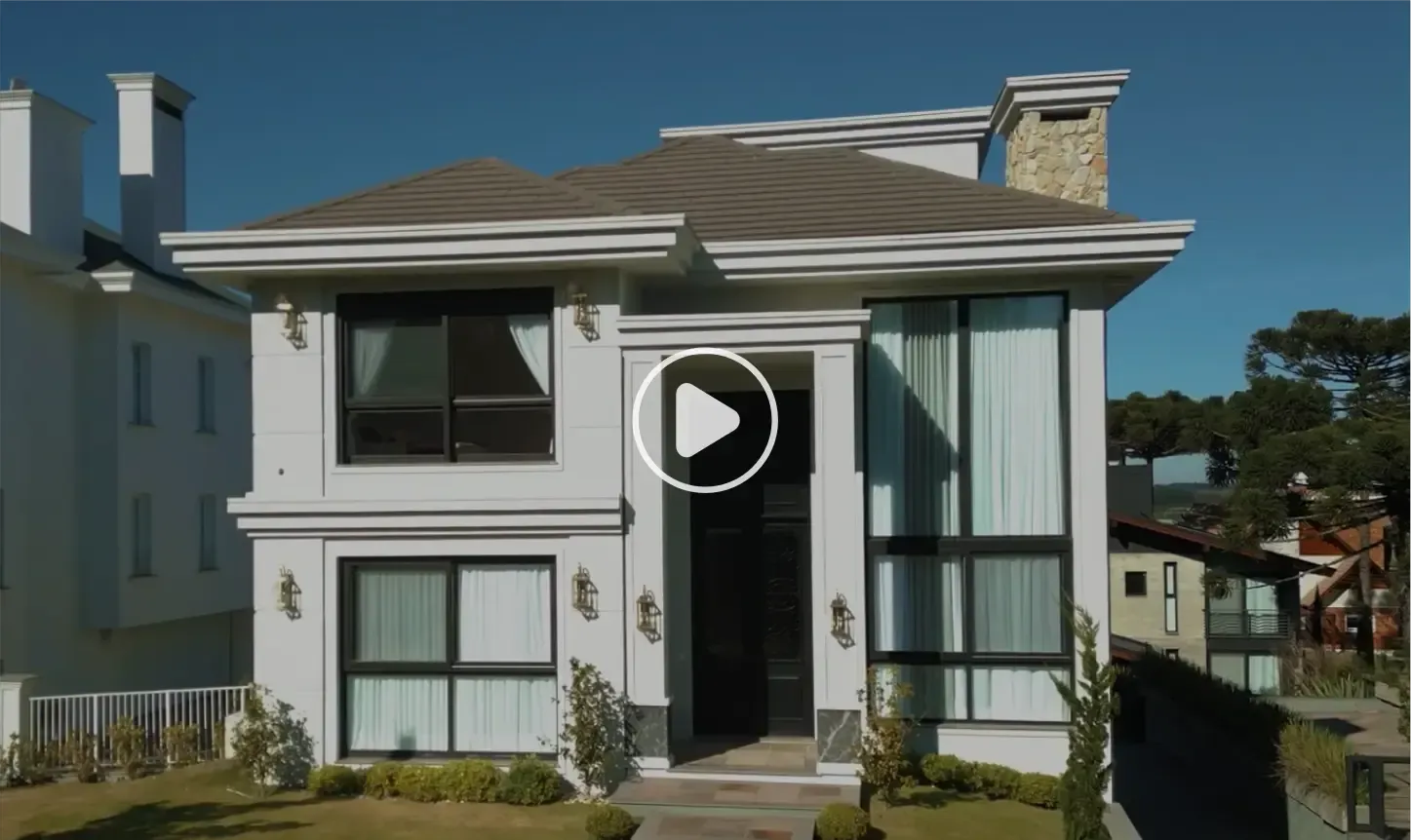 Casa branca de dois andares com janelas grandes, detalhes escuros e chaminé de pedra; céu azul.