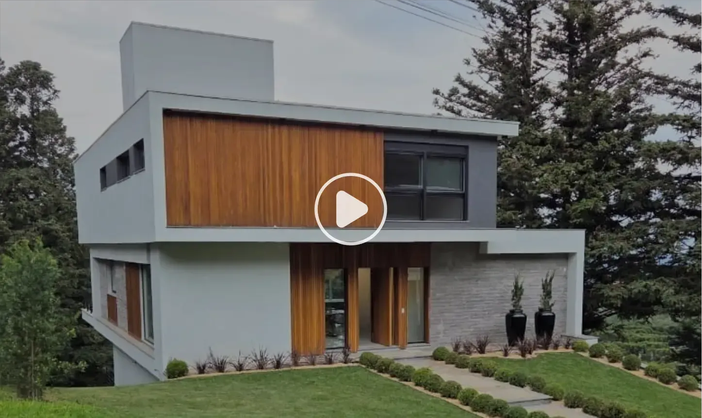 Casa moderna de dois andares com painéis de madeira, paredes cinza e fachada de pedra. Situada em um gramado verdejante.