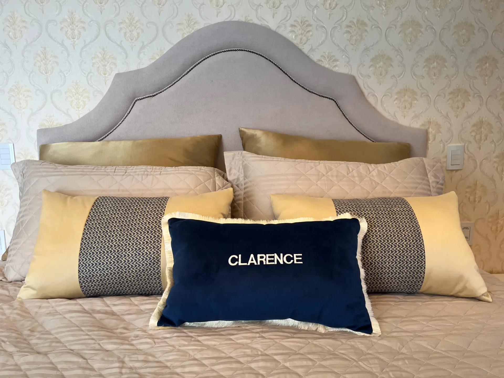 Cama com almofadas decorativas e uma almofada azul-marinho com a inscrição 