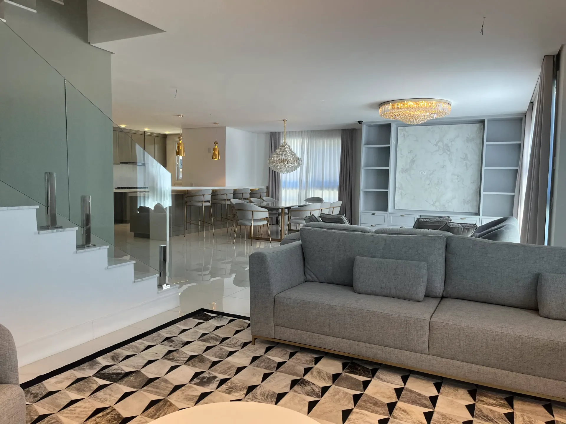 Sala de estar moderna e espaçosa com sofá cinza, cozinha americana e escada.